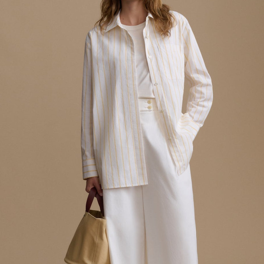 Woman in a white outfit holding a gold handbag against a beige background
