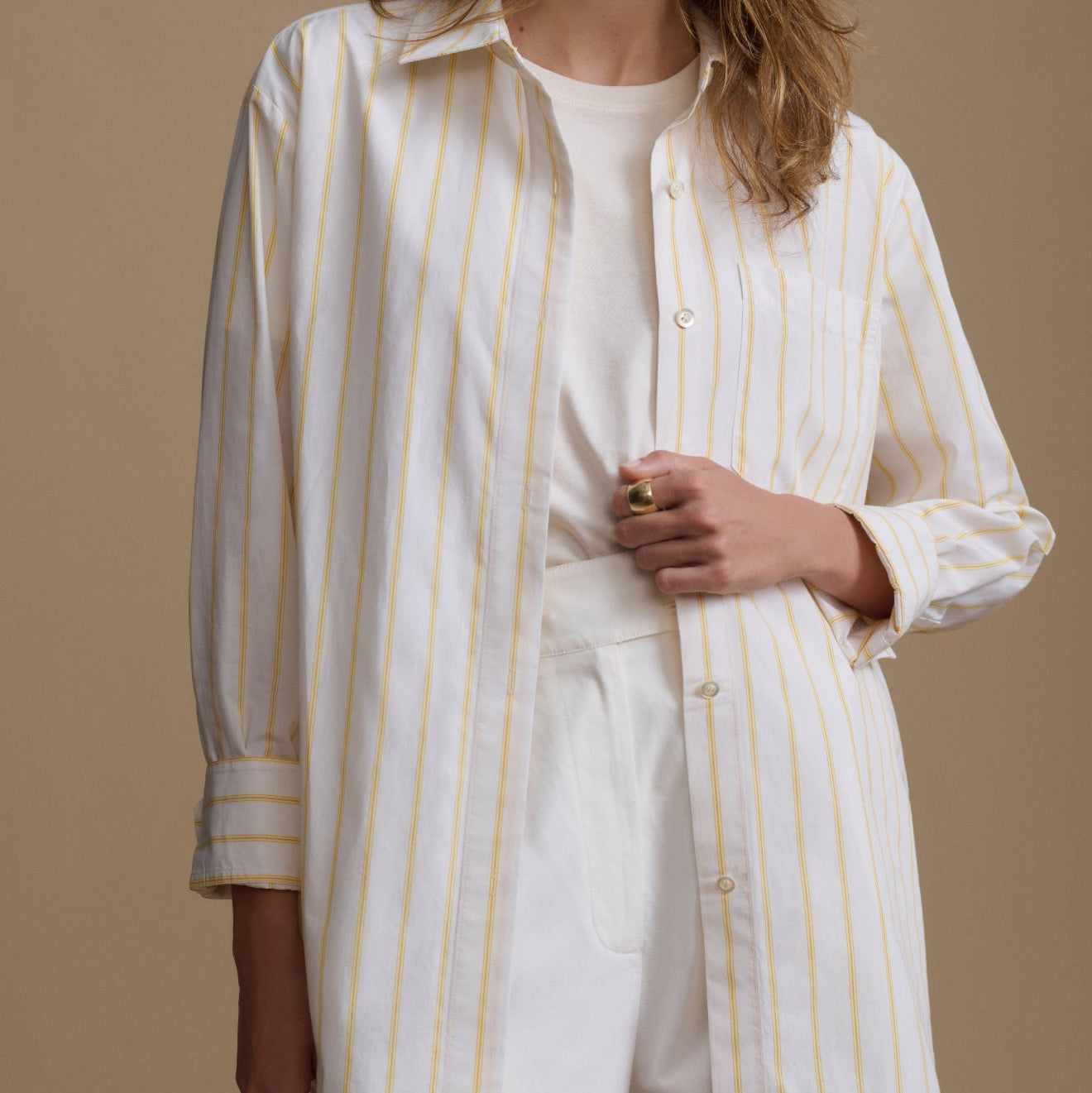Person wearing a white shirt with yellow stripes and white pants on a brown background