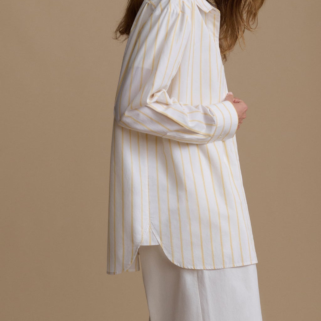 Woman wearing a white and yellow striped shirt against a beige background