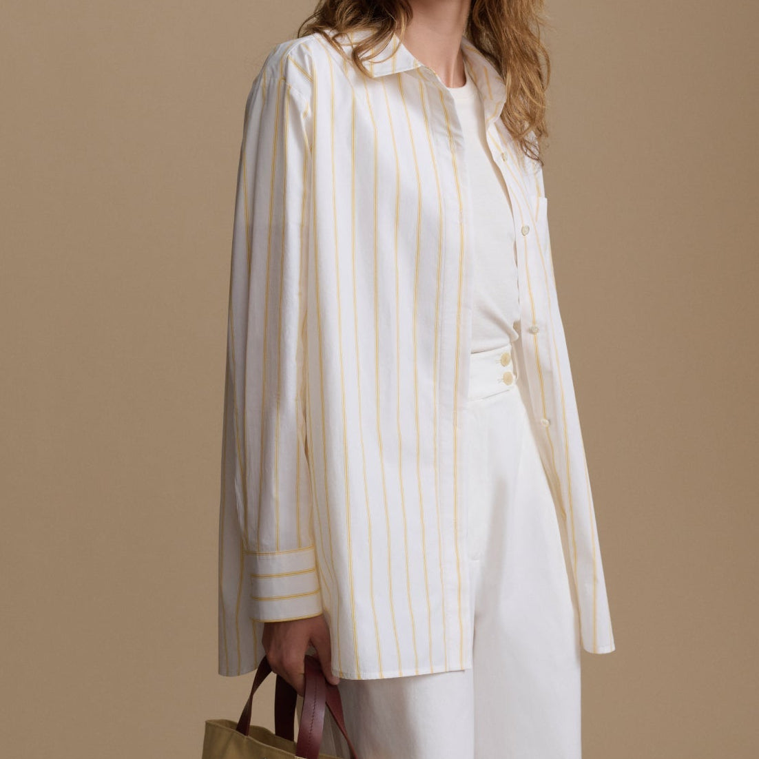Woman wearing a white outfit with yellow stripes against a beige background