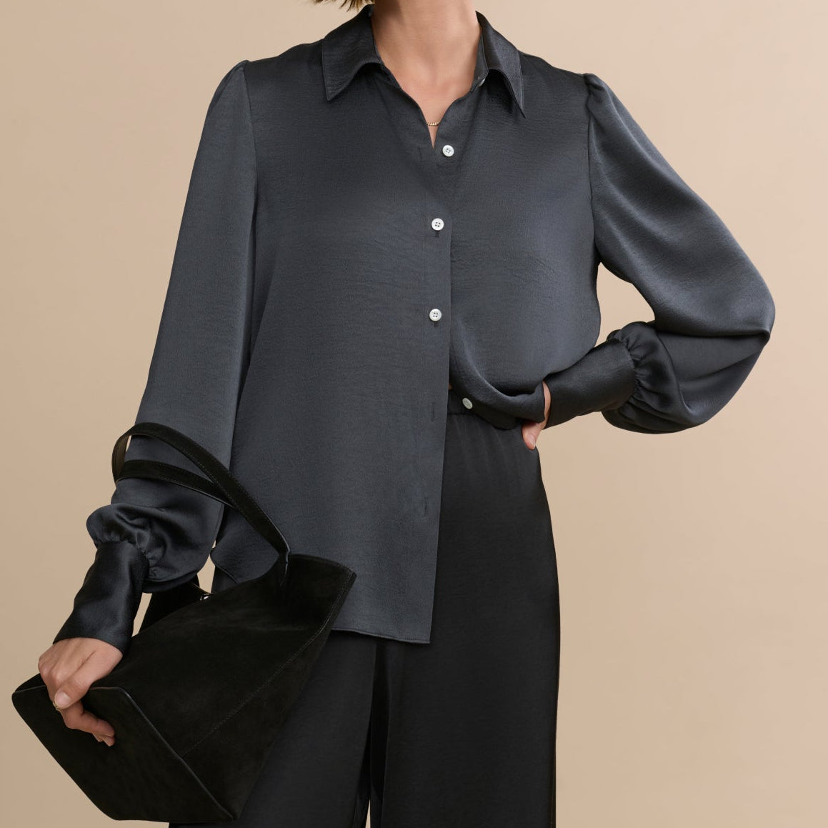 Woman wearing a dark gray blouse with puffed sleeves against a beige background