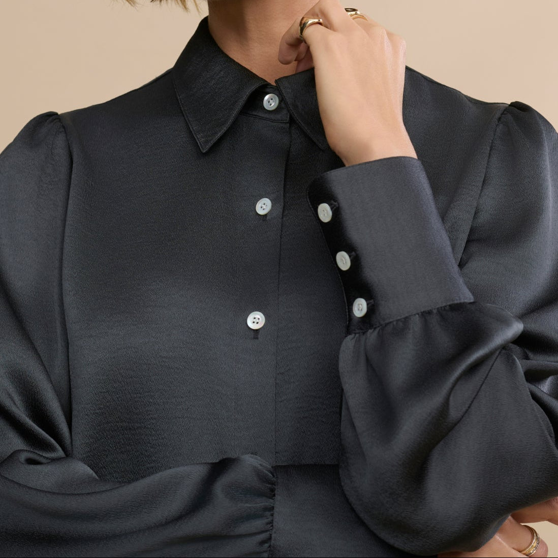 Woman wearing a black blouse with white buttons against a beige background