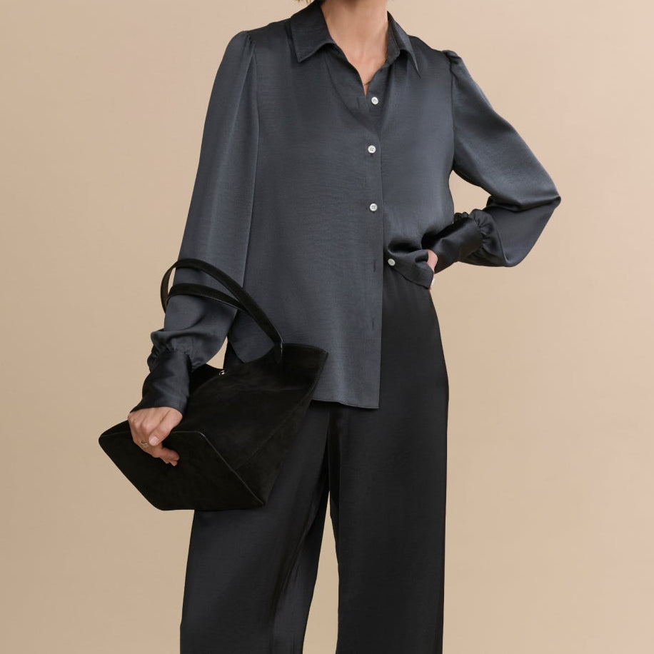 Woman wearing a dark gray blouse and black pants against a beige background