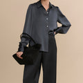 Woman wearing a dark gray blouse and black pants against a beige background