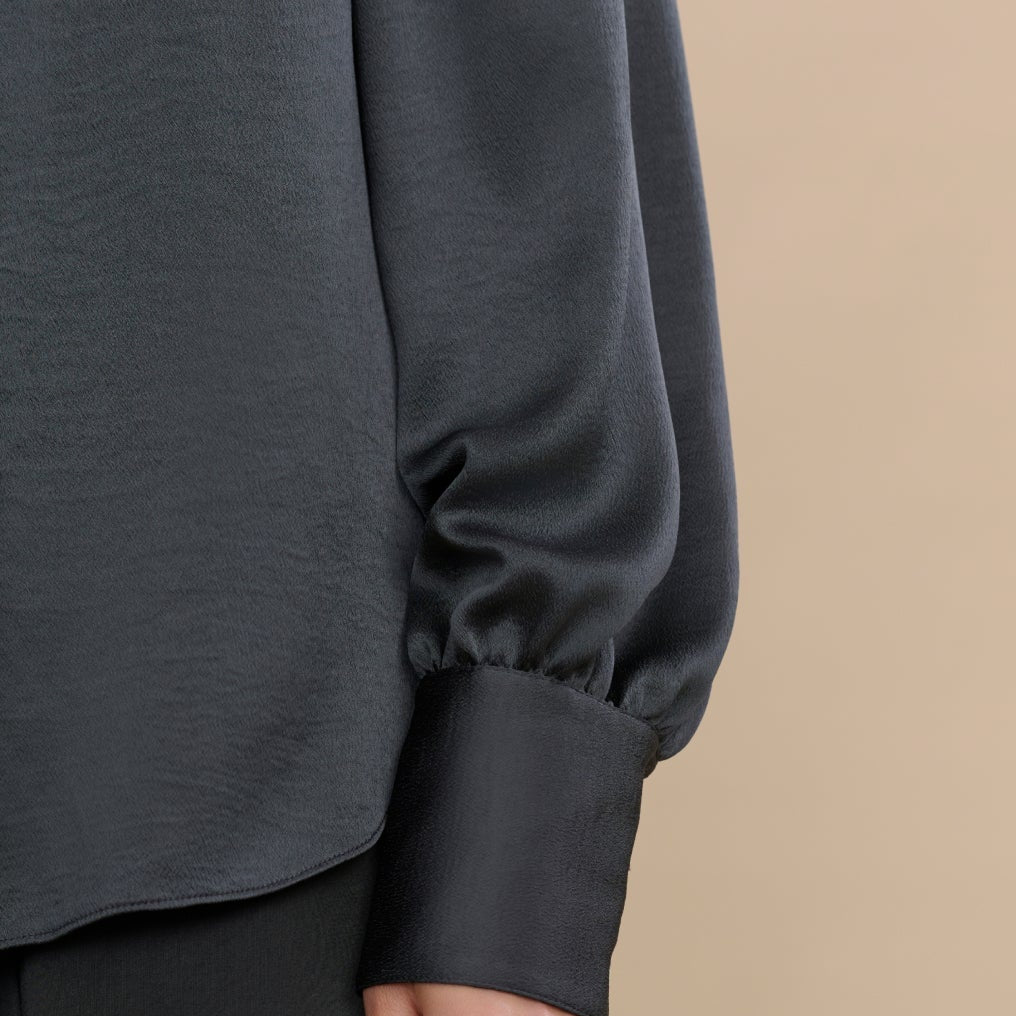 Dark gray long-sleeve top worn by a person on a beige background