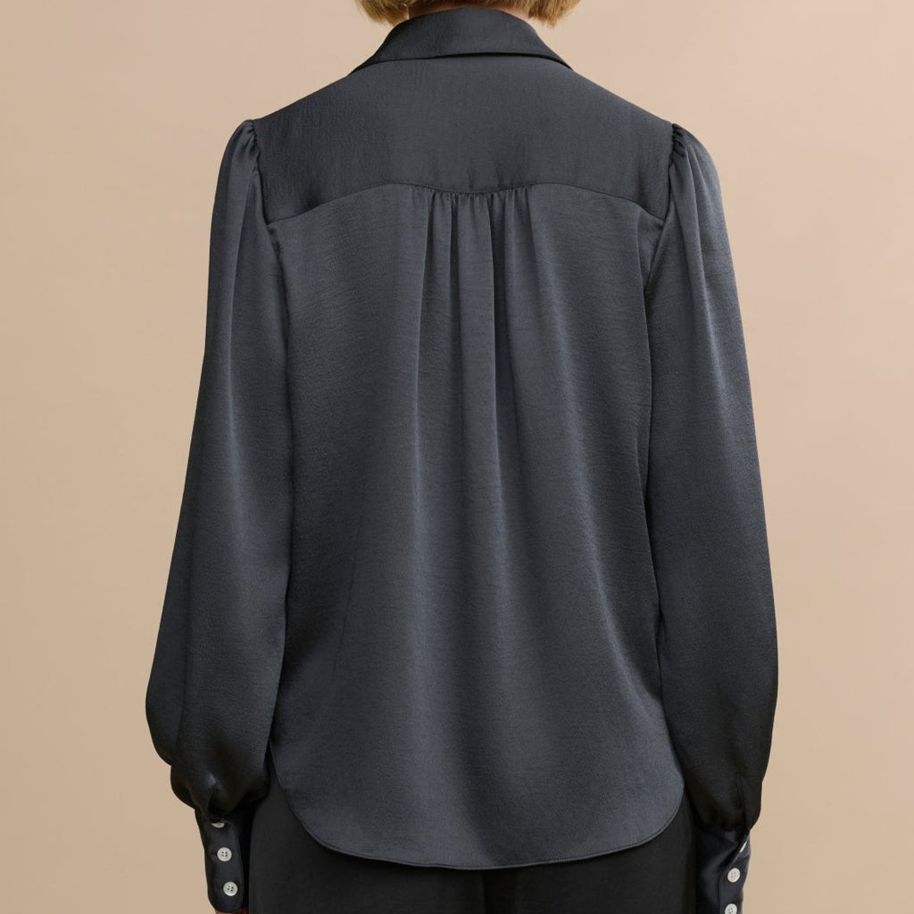 Person wearing a dark gray blouse with long sleeves on a beige background