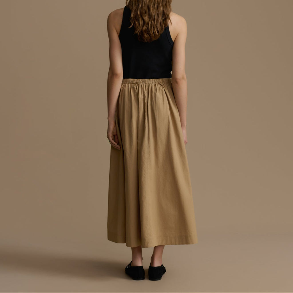Woman wearing a black top and tan skirt against a brown background