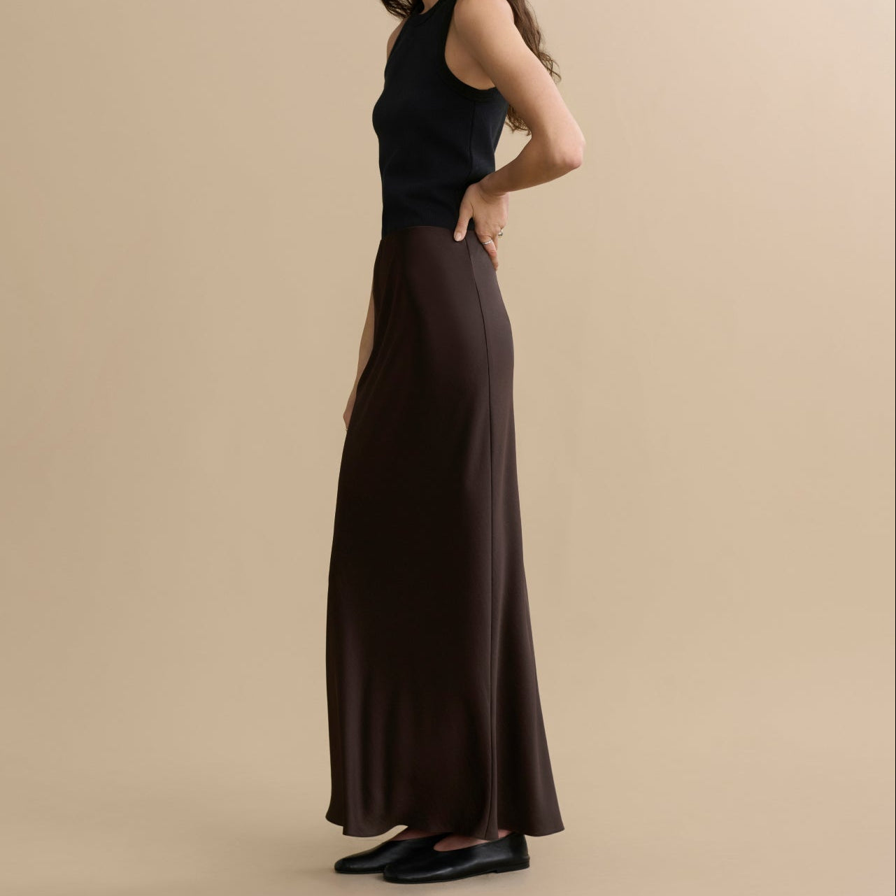 Woman wearing a black sleeveless top and brown skirt against a beige background